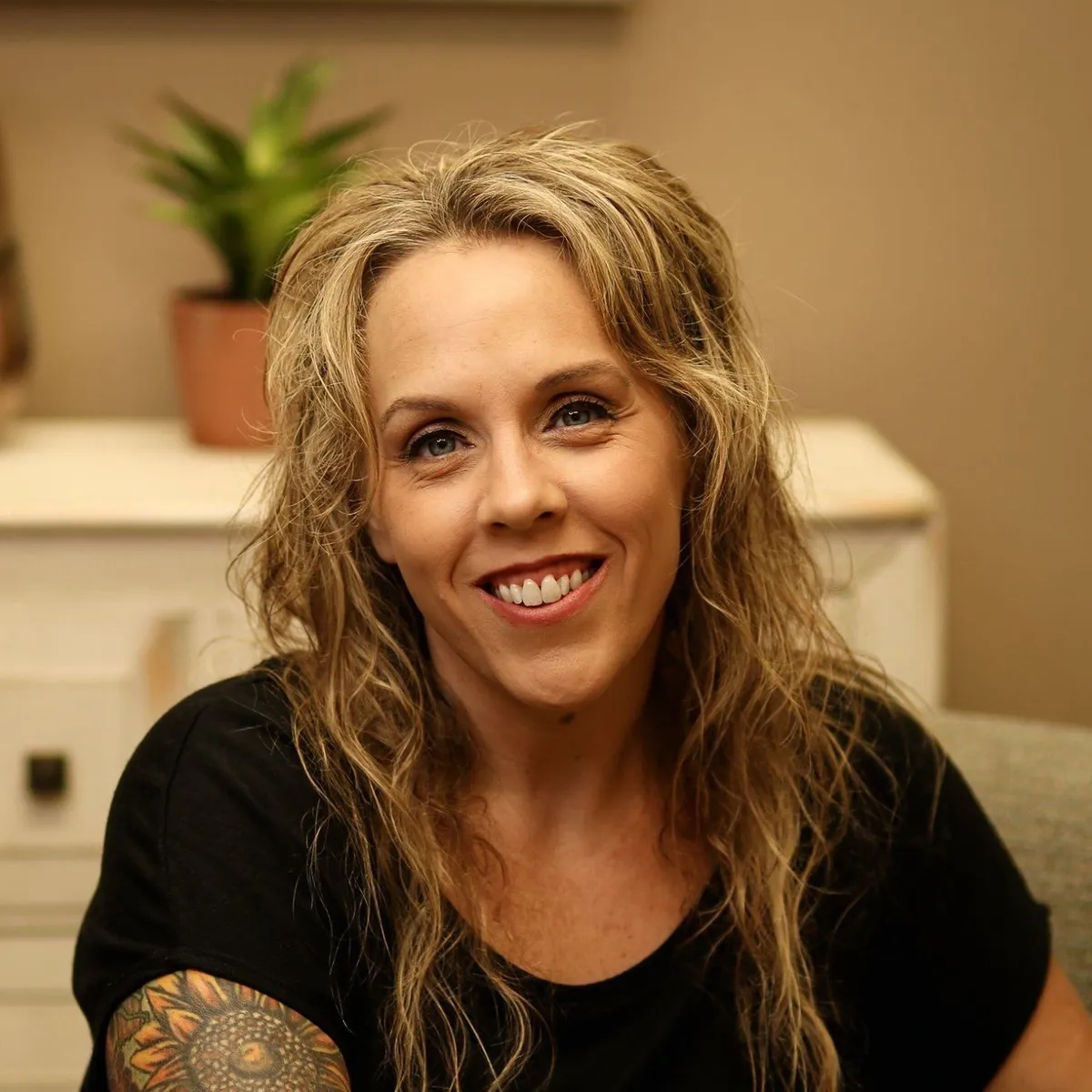 A woman with long hair and tattoos sitting in front of a desk.